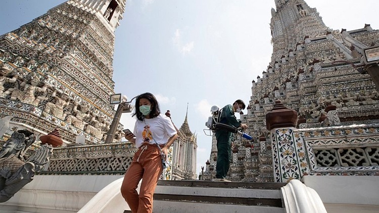 Khách du lịch đeo khẩu trang tham quan một ngôi chùa tại Bangkok trong lúc công nhân phun thuốc khử trùng ngày 12/3. Ảnh: AP